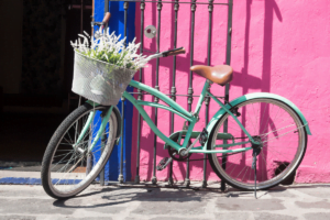 bicicleta verde con una cesta en el mainillar con flores delante de una pared rosa